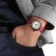 Person wearing a watch with a red strap and black and white face.