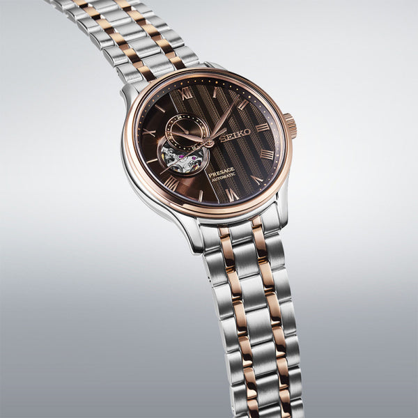 Seiko watch with two-tone metal strap on gray backgroundGents Seiko Presage Japanese Garden Automatic Watch. The 41.8mm case and bracelet are bicolour: rose gold PVD and stainless steel. The dial is black with a textured pattern, rose coloured roman numerals and hands, 24-hour indicator sub-dial and circular shaped movement window. The watch has a sapphire crystal glass with a see-through case back. The movement is automatic. MODEL SSA466J