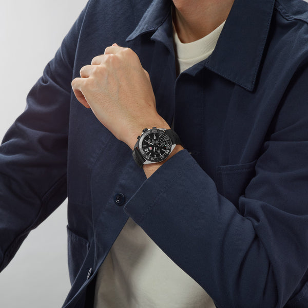 Person wearing a dark blue jacket with a watch on their wrist against a light background