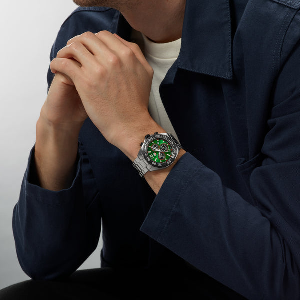 Person wearing a watch with a green face on a plain background