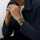 Person wearing a watch with a green face on a plain background