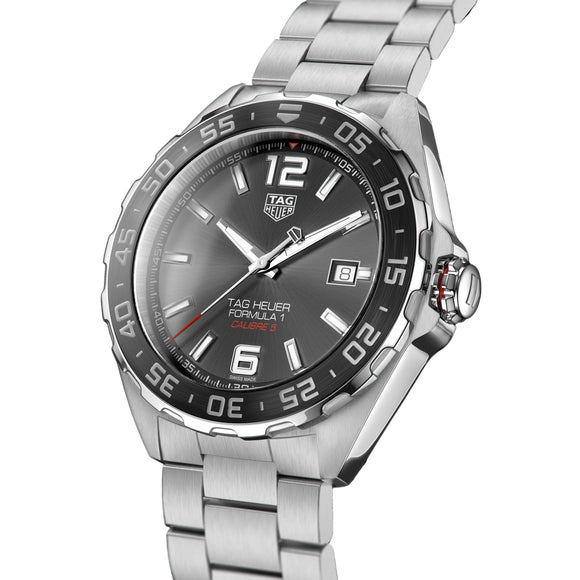 A silver stainless steel wristwatch with a dark gray dial, featuring a black rotating bezel with white markings, silver-tone hour markers, and a date window at 3 o'clock. The watch is shown at a three-quarter angle against a solid black background, with the brand name 'TAG HEUER' visible on the dial.