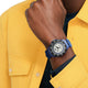 Person wearing a blue watch with a white face on a yellow shirt background